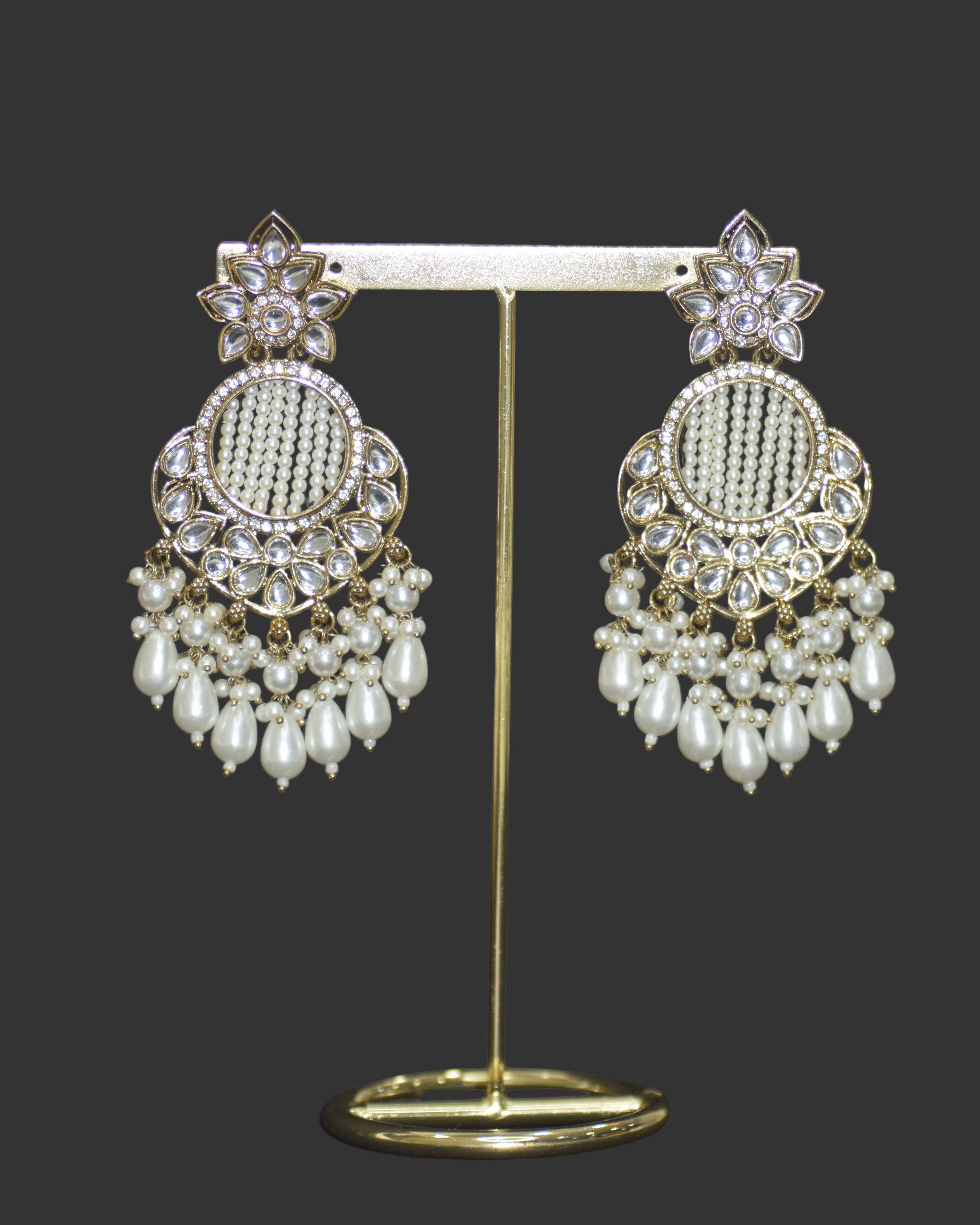 Pair of ornate earrings with gold and pearl details on a dark background