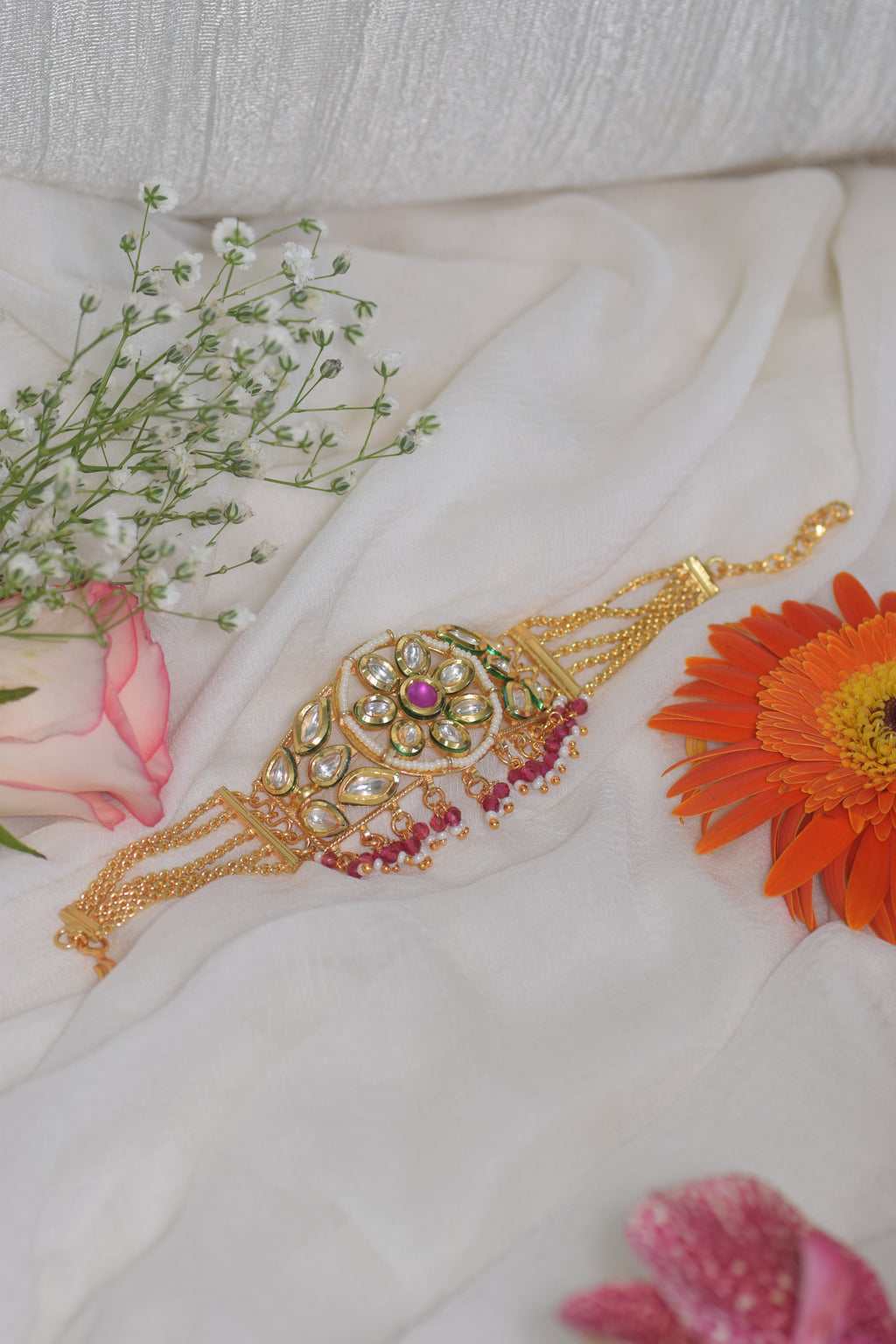 Decorative gold bracelet with gemstones on a white fabric background with flowers.