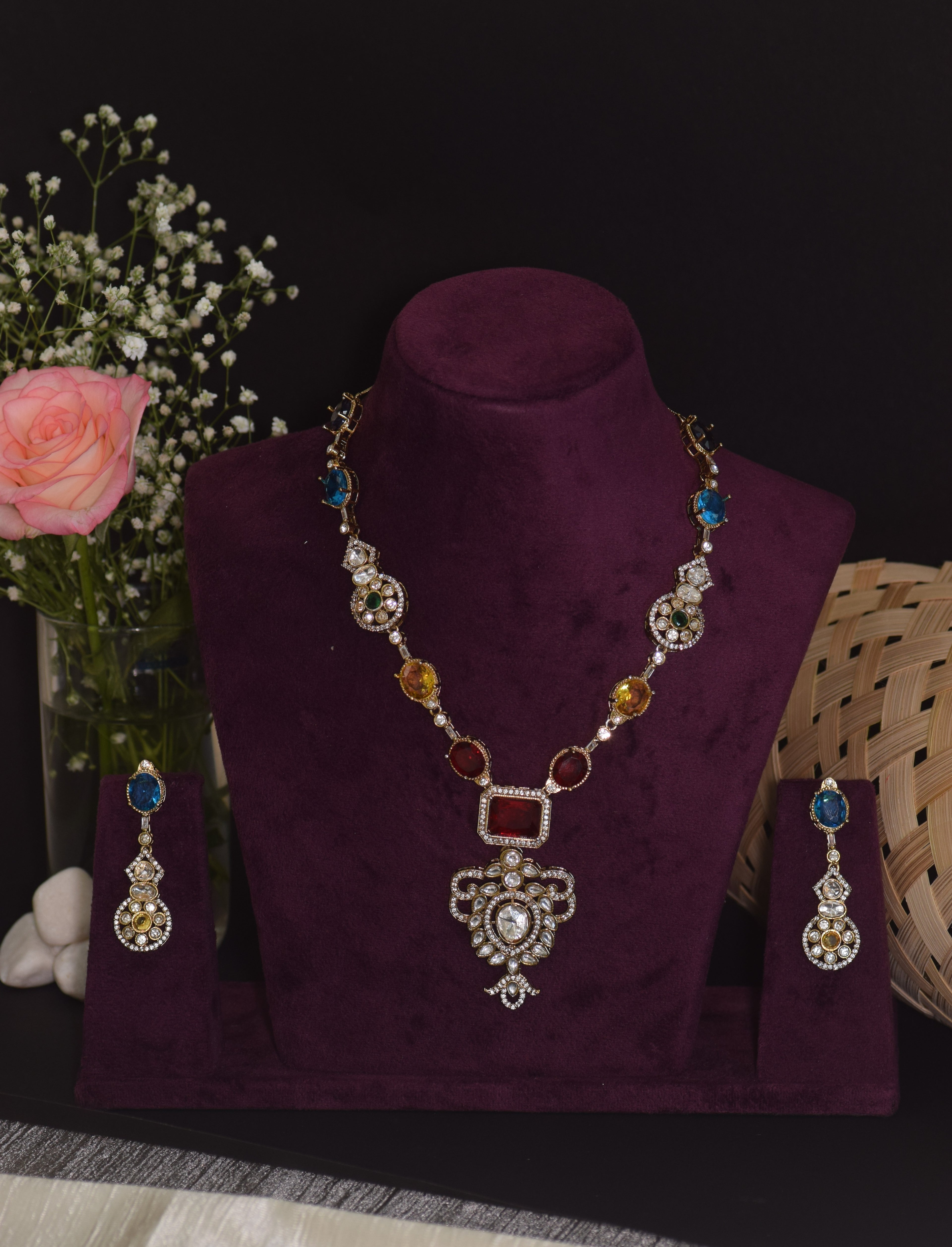 Jewelry set with necklace and earrings on a purple stand, flowers and basket in the background.