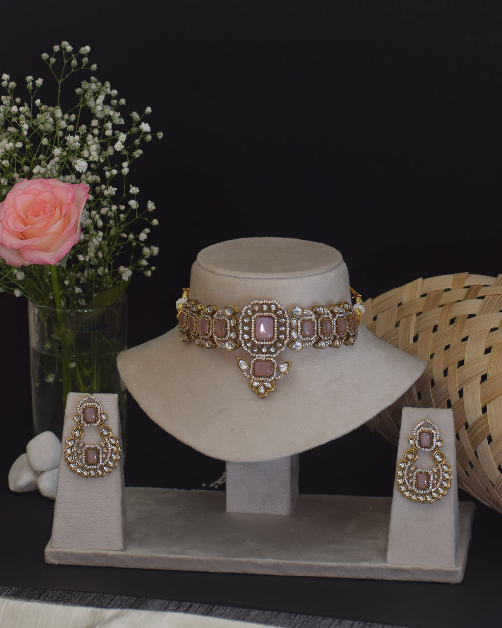 Gold jewelry set with a bracelet and earrings on a white stand, accompanied by a small bouquet of flowers.
