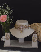 Gold jewelry set with a bracelet and earrings on a white stand, accompanied by a small bouquet of flowers.