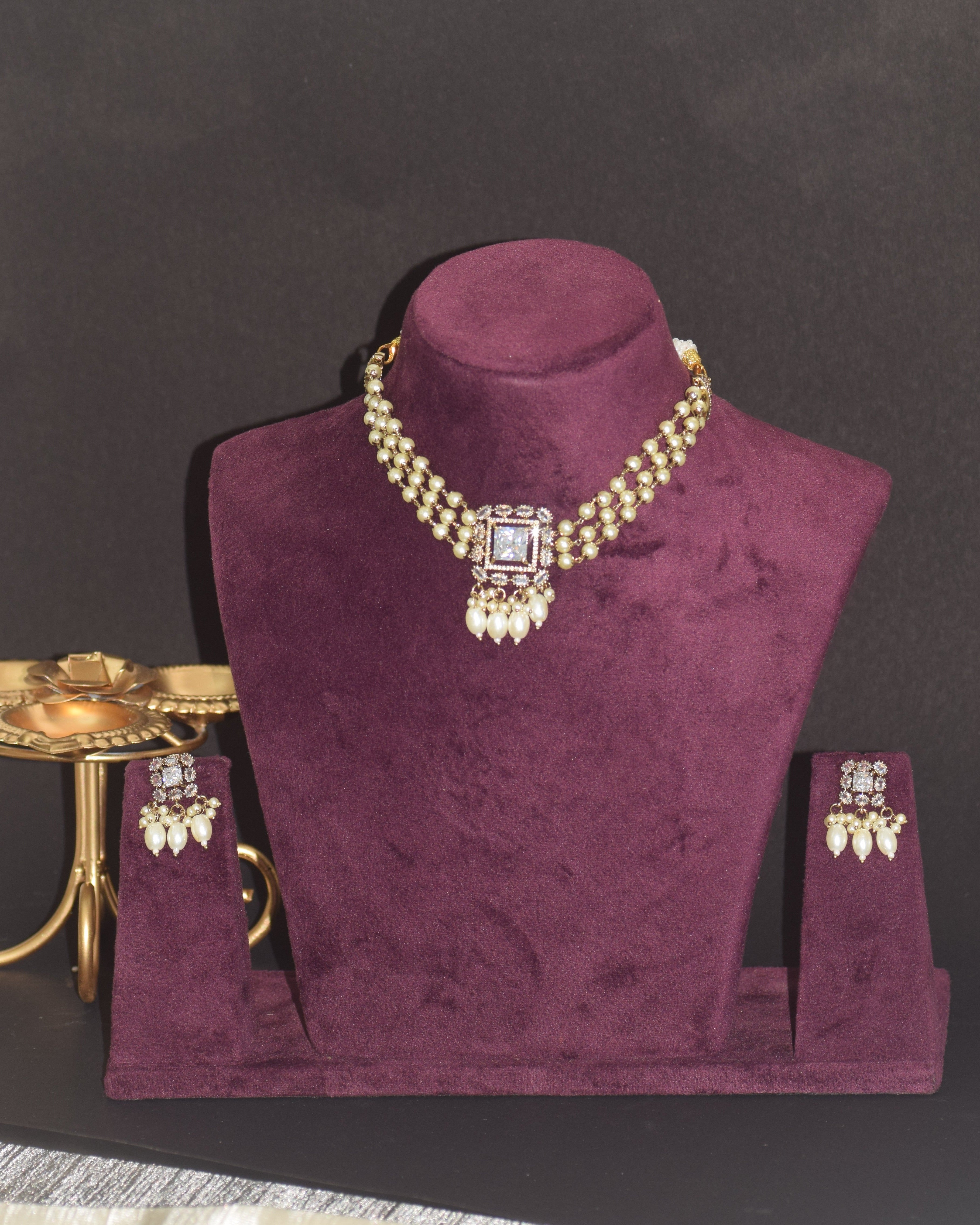 Gold necklace and earrings on a purple velvet stand against a dark background
