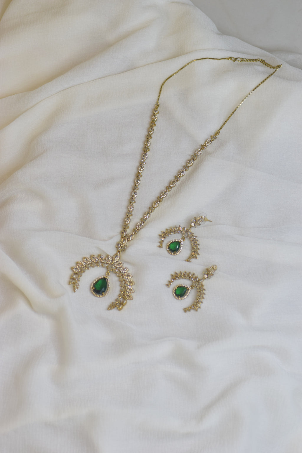 Gold necklace and earrings with green gemstones on a white fabric background