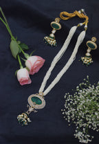Decorative necklace with green and gold elements on a dark fabric background with flowers.