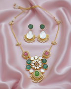 Ornate necklace with green and pink stones on a pink fabric background
