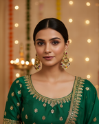 Woman wearing a green traditional outfit with gold embroidery against a softly blurred background.