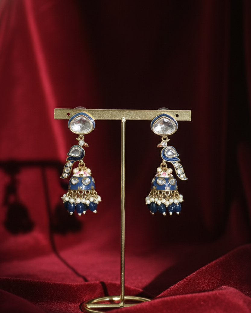 Pair of blue and gold earrings on a stand against a red fabric background