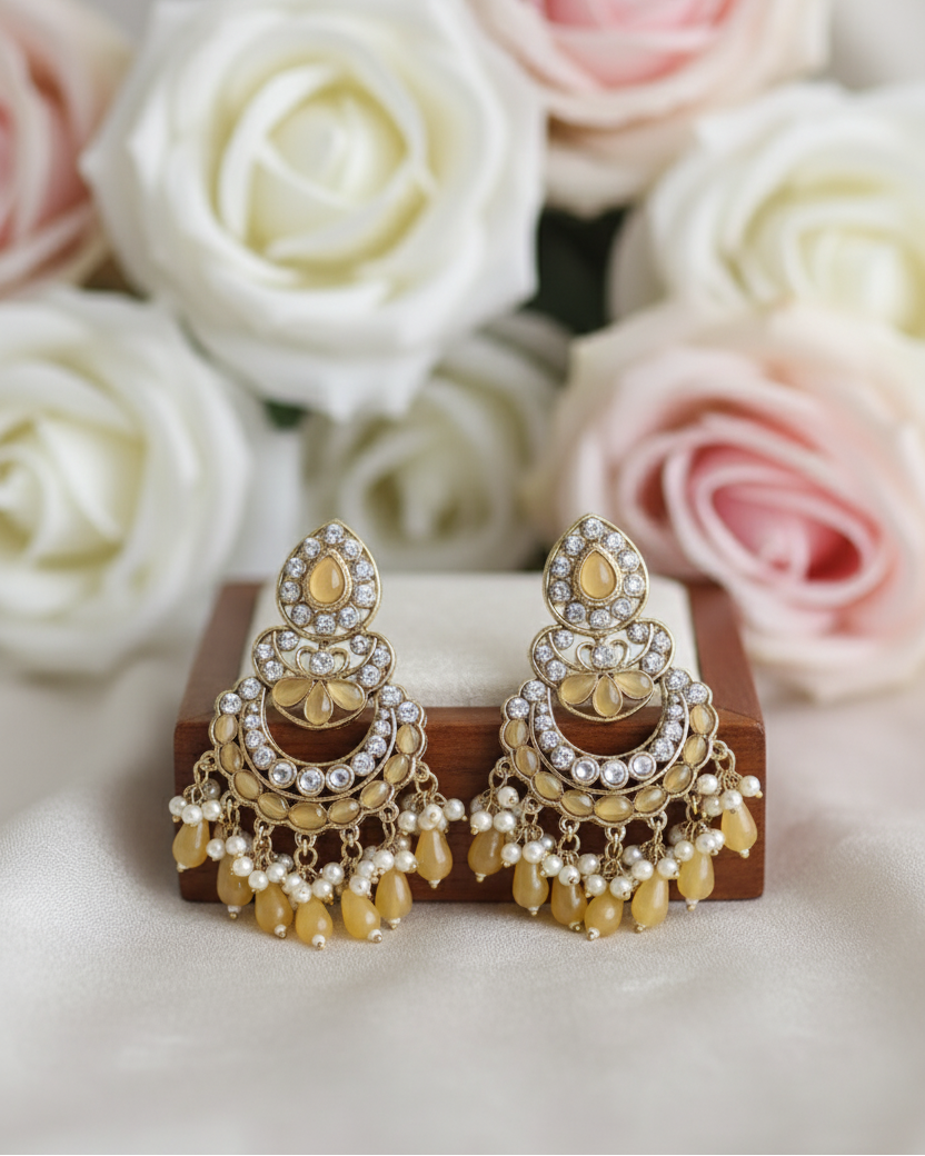 Gold earrings on a wooden stand with pink and white roses in the background