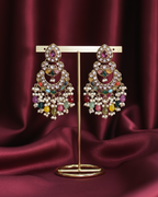 Colorful gemstone earrings on a gold stand against a burgundy fabric background