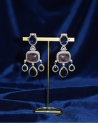 Pair of ornate earrings on a gold stand against a blue fabric background