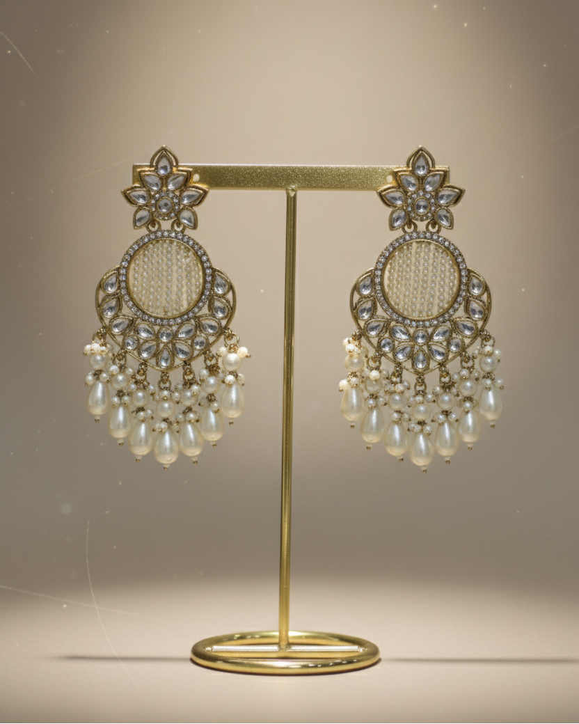 Pair of ornate earrings on a gold stand against a neutral background