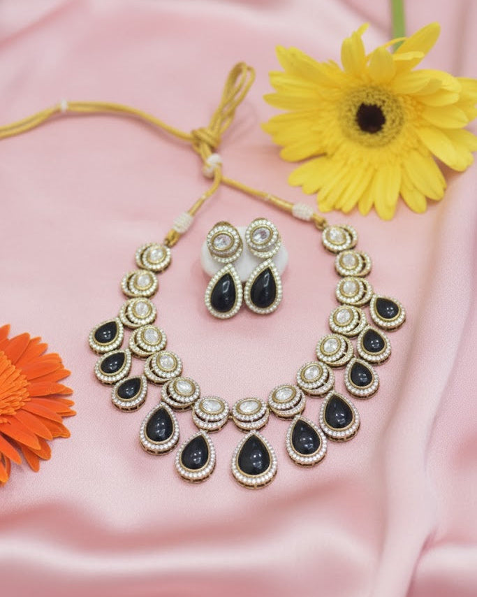Ornate necklace and earrings with black and gold accents on a pink fabric background with flowers.