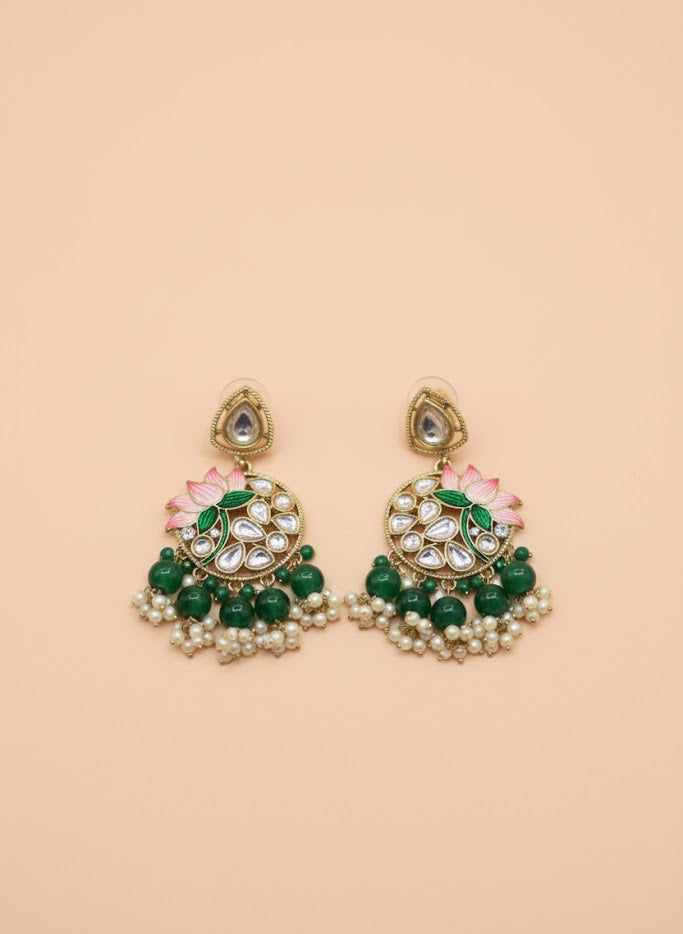 Pair of green and gold earrings with floral designs on a beige background
