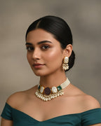 Woman wearing a green off-shoulder top and a necklace with earrings against a neutral background