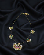 Gold necklace with green and red gemstones on black satin fabric