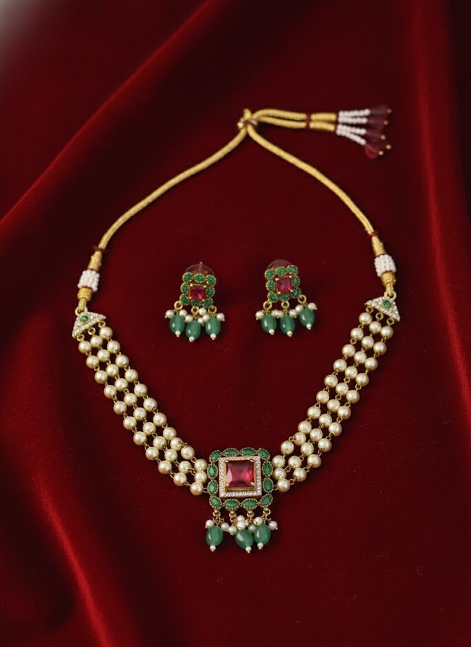 Gold necklace with green and red gemstones on a red velvet background