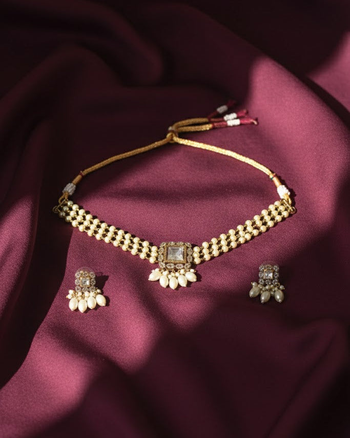Gold necklace and earrings set on a maroon fabric background