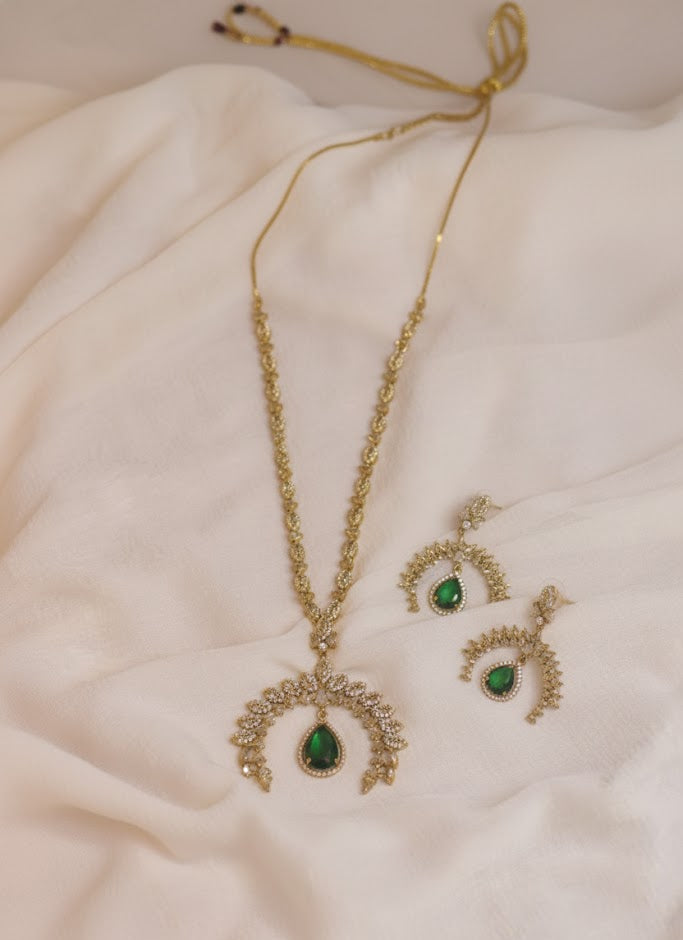 Gold necklace and earrings with green gemstones on a soft fabric background
