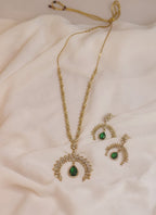 Gold necklace and earrings with green gemstones on a soft fabric background