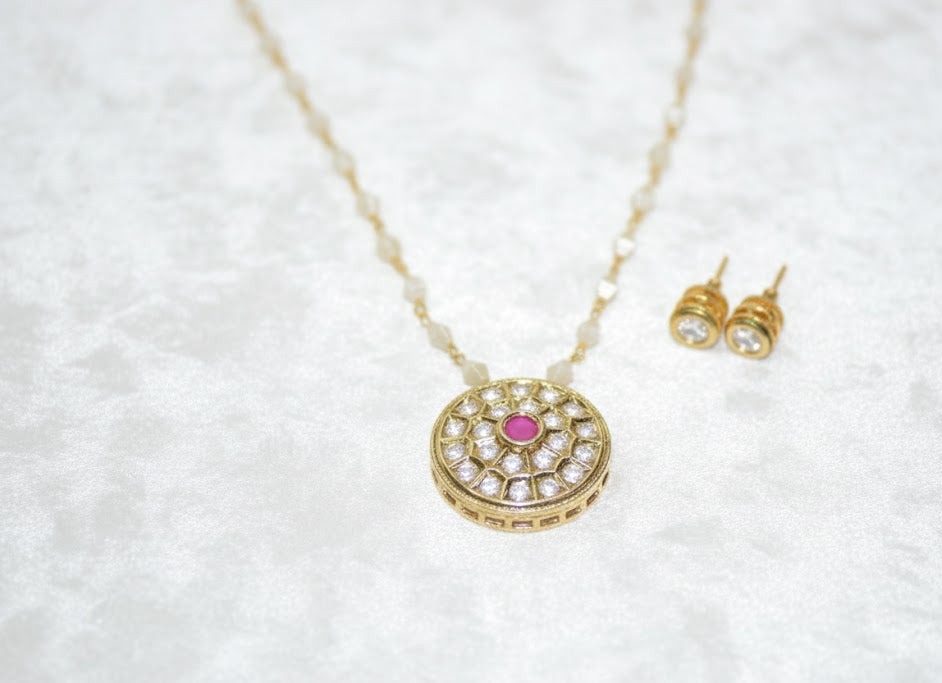 Gold necklace with pink gemstone and matching earrings on a white textured background