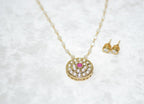 Gold necklace with pink gemstone and matching earrings on a white textured background